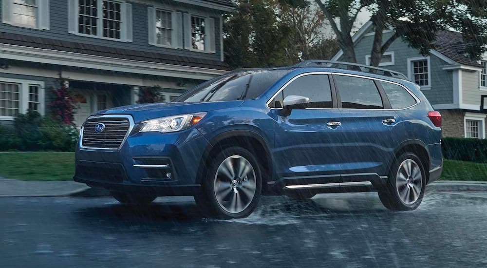 A blue 2021 Subaru Ascent is shown driving through the rain in a suburban neighborhood.