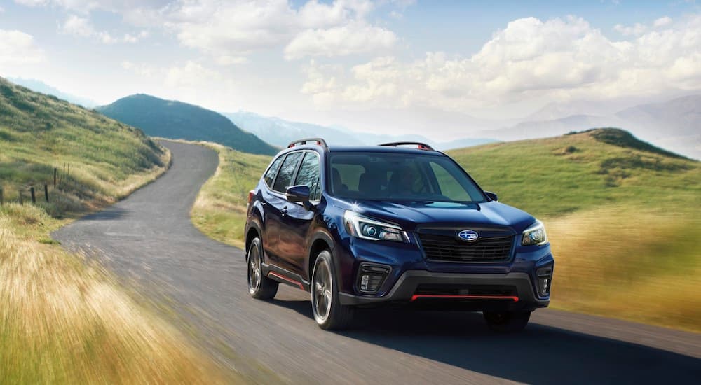 A dark blue 2021 Subaru Forester is shown driving over rollings hills.