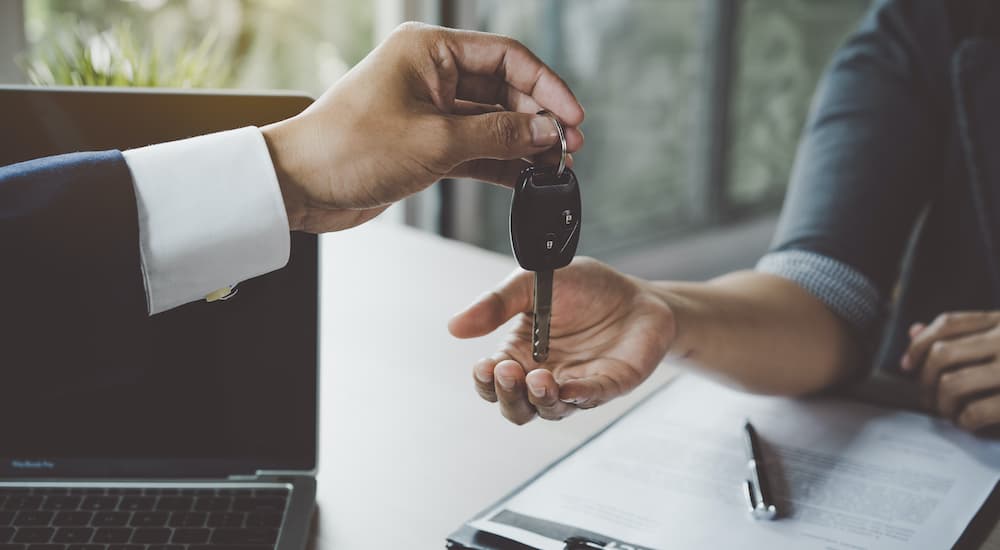 A set of keys is shown being exchanged over paperwork at a dealership with used trucks for sale.