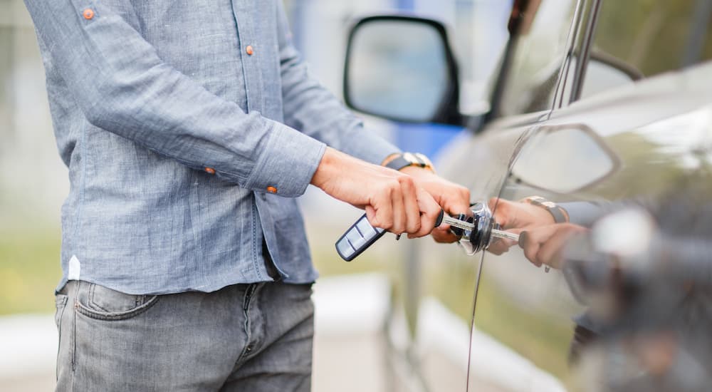 A close up shows a person unlocking a car door at a used car dealership.