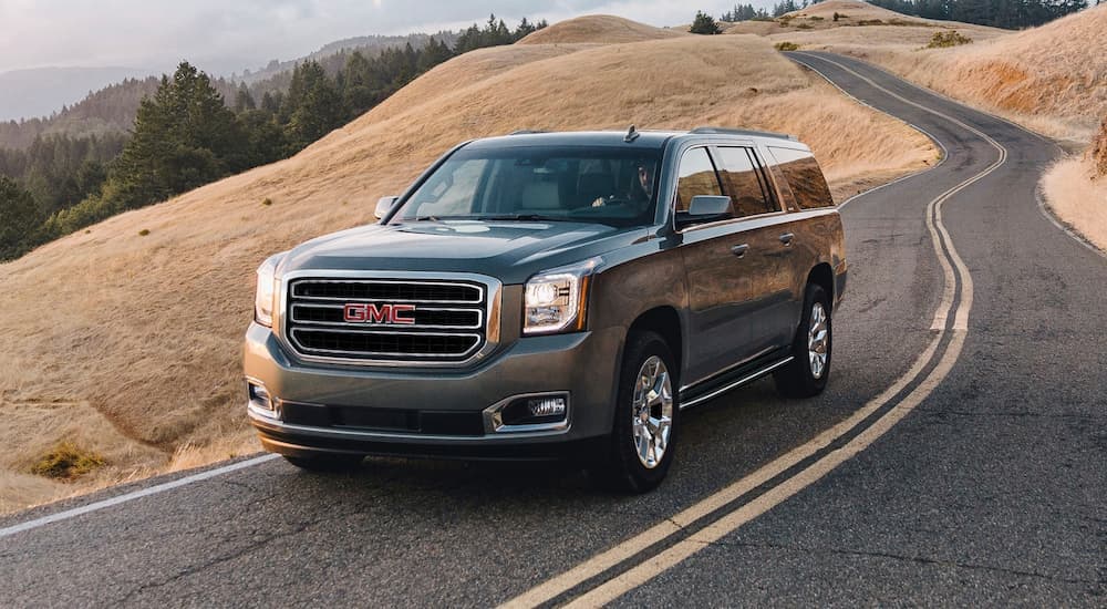 A grey 2020 GMC Yukon is shown from the front driving down a two lane road.