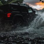 A black 2020 Jeep Wrangler Unlimited is shown driving through a river after leaving a used car deaership.