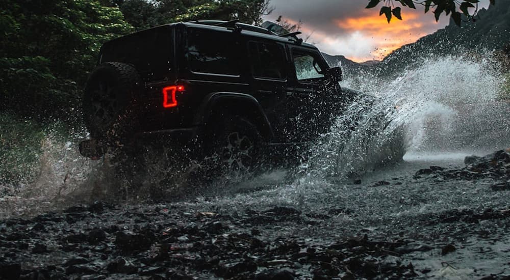 A black 2020 Jeep Wrangler Unlimited is shown driving through a river after leaving a used car deaership.