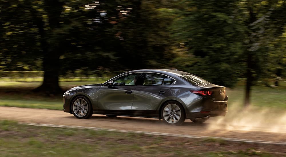 A grey 2020 Mazda3 is shown from the side driving down a dirt road.