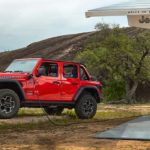 A red 2021 Jeep Wrangler 4xe is shown charging in a rural location.