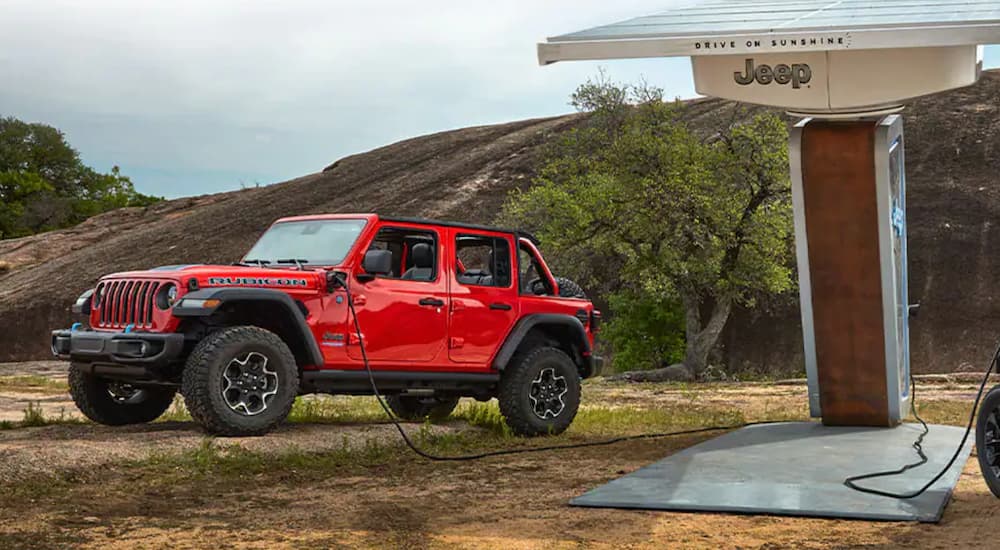 A red 2021 Jeep Wrangler 4xe is shown charging in a rural location.