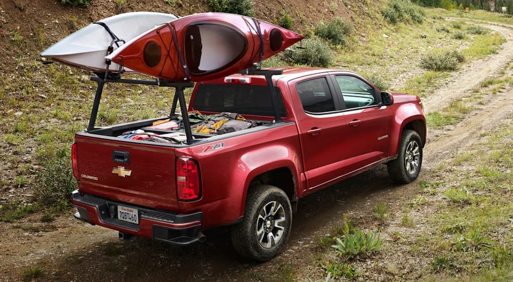 A red 2020 Chevy Colorado is shown driving on a dirt road with two kayaks on the back.