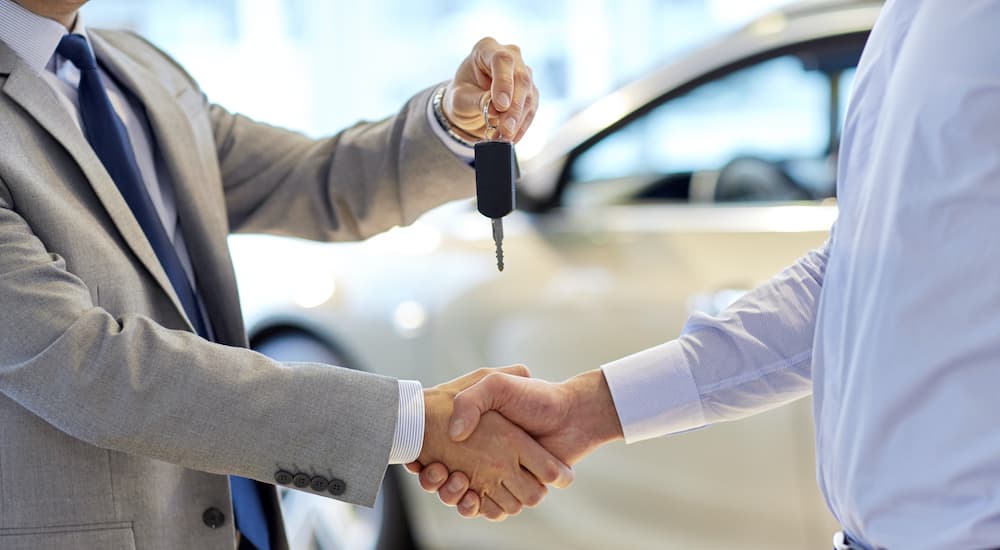 A salesman is shaking hands with a person at a used car dealership.
