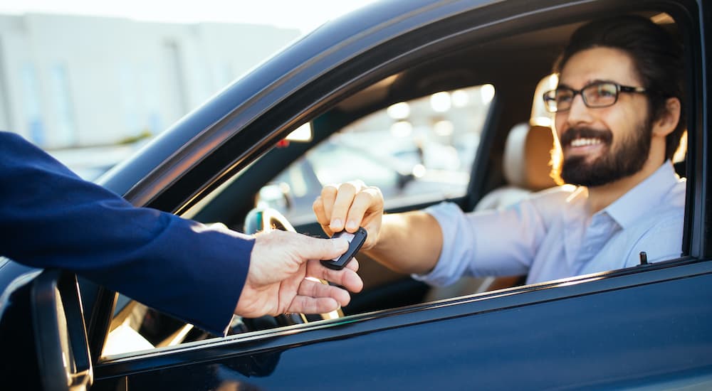 A man is sitting in the front seat of a car as a salesperson passes a set of keys.