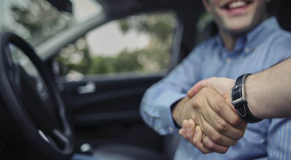A salesman is shaking the hand of a driver after telling them where to buy used cars.