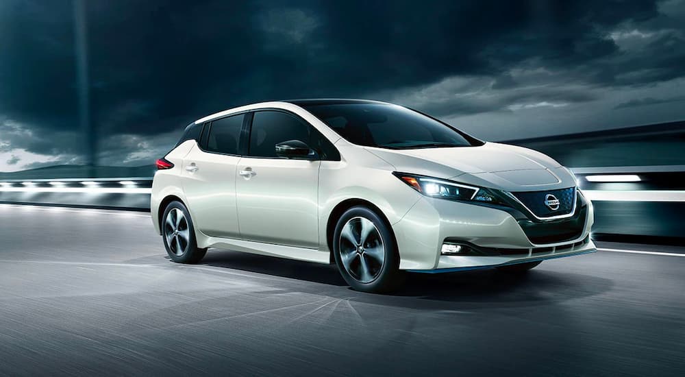 A silver 2019 Nissan Leaf is shown driving on an empty road with a cloudy night sky.