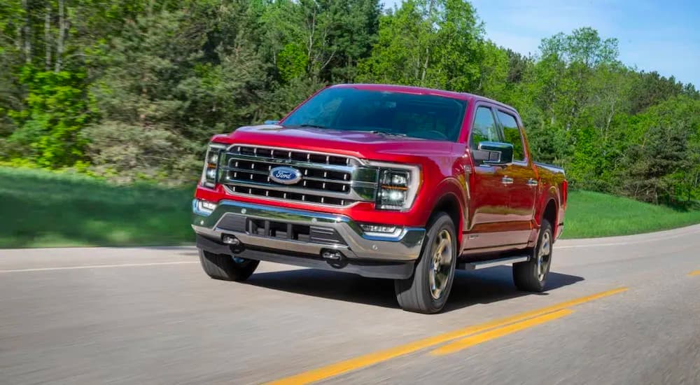 A red 2021 Ford F-150 is shown driving down a wooded road.
