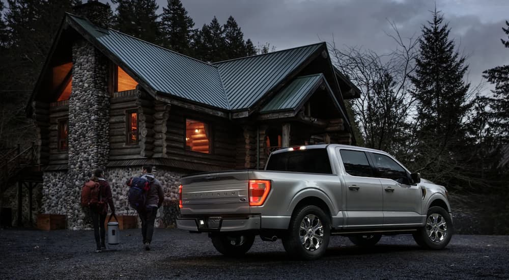 A silver 2021 Ford F-150 Platinum is shown from the rear parked near a cabin at night.