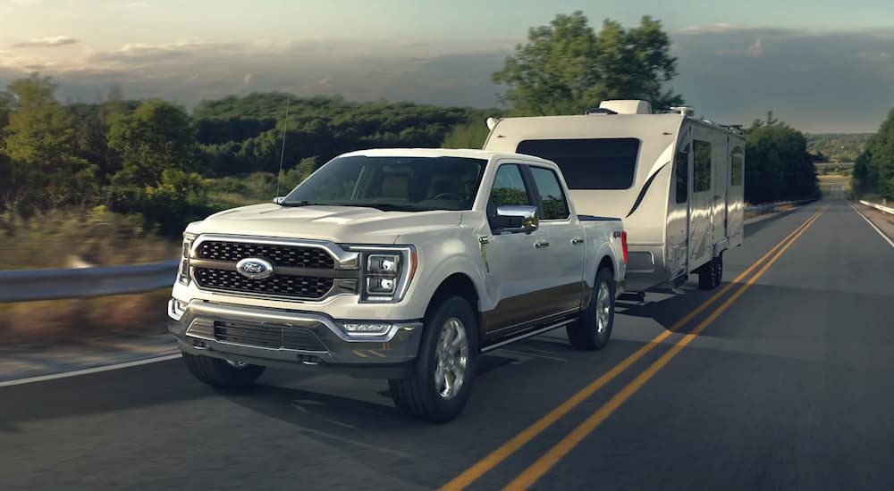 A white 2021 Ford F-150 is shown towing a trailer down a road.