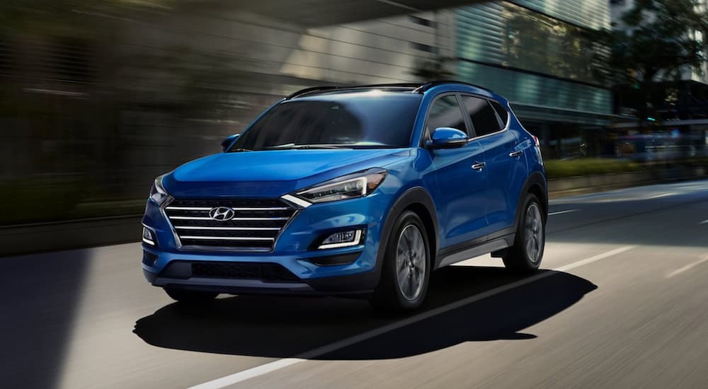 A blue 2021 Hyundai Tucson is shown from the front driving through a city.