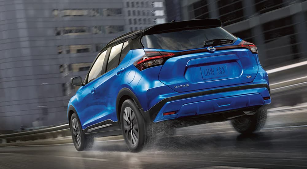 A blue 2021 Nissan Kicks is shown from the rear driving through a city.