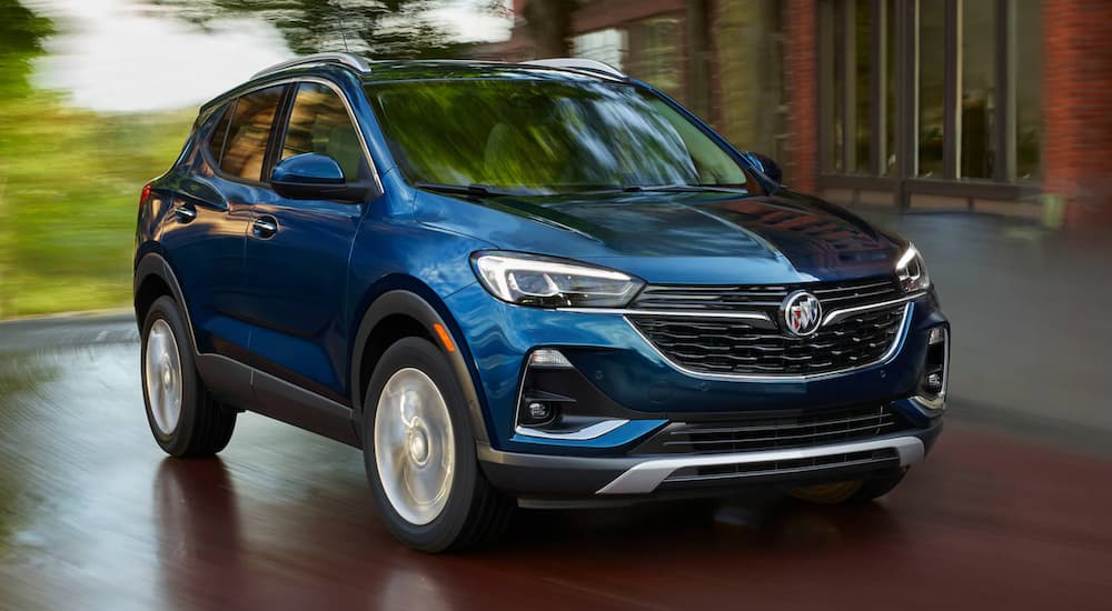 A blue 2022 Buick Encore GX is shown form the front driving past a modern house.