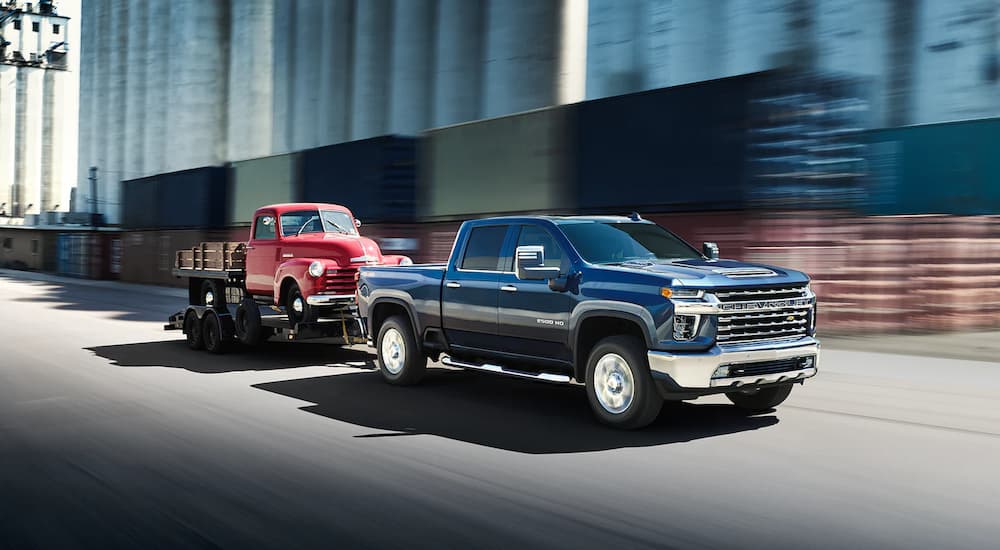 A blue 2022 Chevy Silverado 2500HD is shown towing a red truck on a trailer.