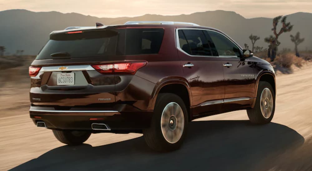 A maroon 2022 Chevy Traverse is shown from the rear driving on an open road in the desert.