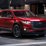 A red 2022 Chevy Traverse is shown stopped at a red light in a city.