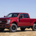 A red Ford 2022 F-250 Lariat is shown from the side parked at a farm.