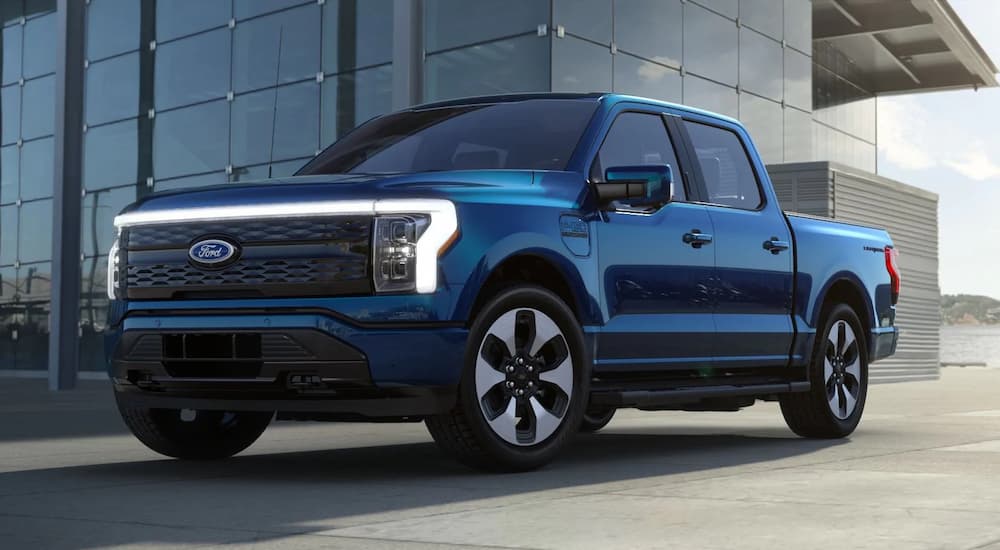 A blue 2022 Ford F-150 Lightning is shown parked next to a building.