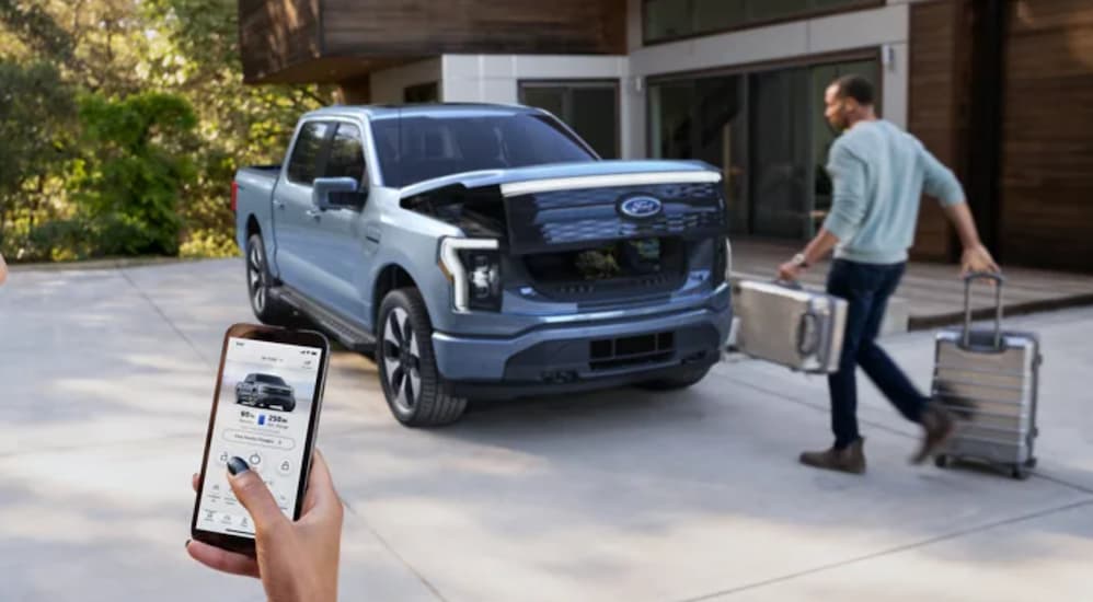 A blue 2022 Ford F-150 Lightning is shown being unlocked with a smartphone.