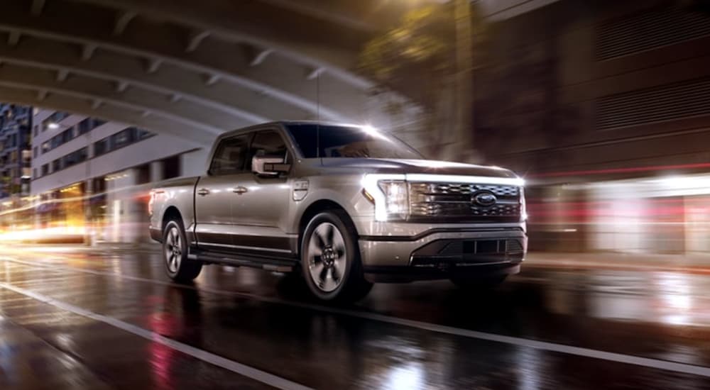 A grey 2022 Ford F-150 Lightning is shown from the side driving through a city at night.