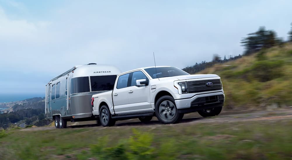 A white 2022 Ford F-150 Lightning is shown towing an airstream on an open road.