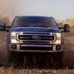 A blue 2022 Ford Super Duty F-250 Lariat is shown from the front driving through a mud puddle.