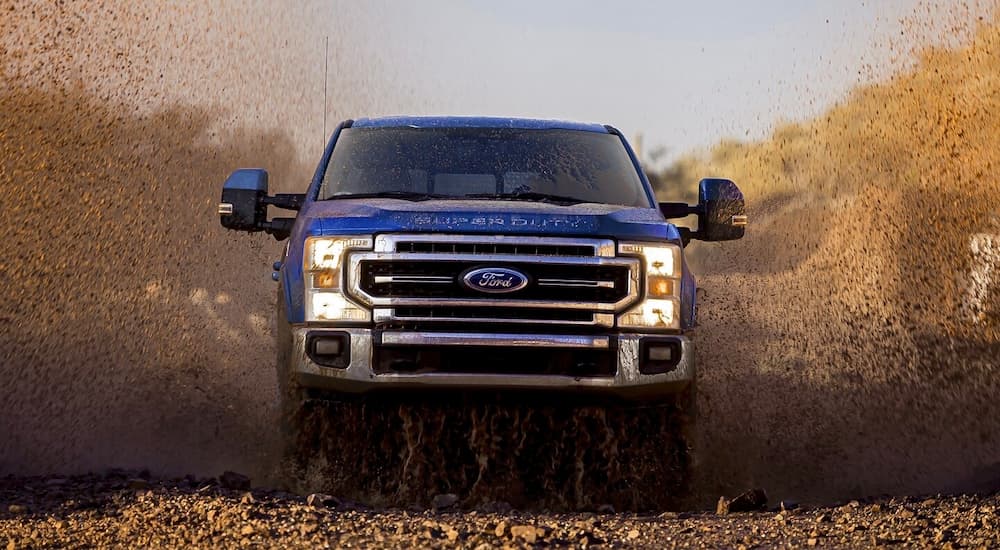 A blue 2022 Ford Super Duty F-250 Lariat is shown from the front driving through a mud puddle.
