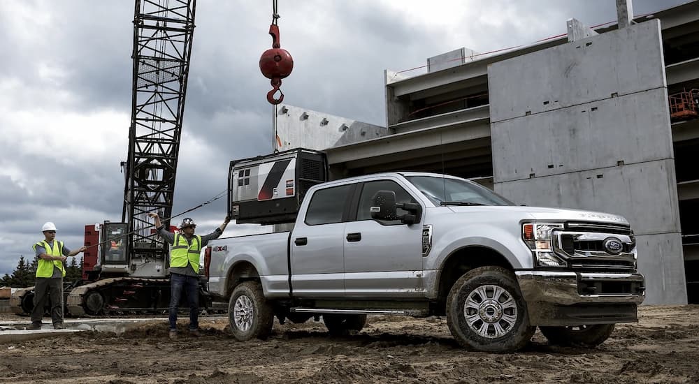 Construction workers are shown lowering a generator into the bed of a silver 2022 Ford Super Duty F-250 with a crane.