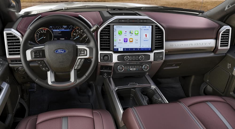 The black and maroon interior of a 2022 Ford Super Duty F-350 Platinum shows the steering wheel and infotainment screen.