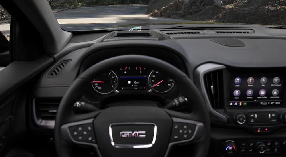 A close up of the black and silver accented interior of a 2022 GMC Terrain AT4 shows the steering wheel and dashboard.