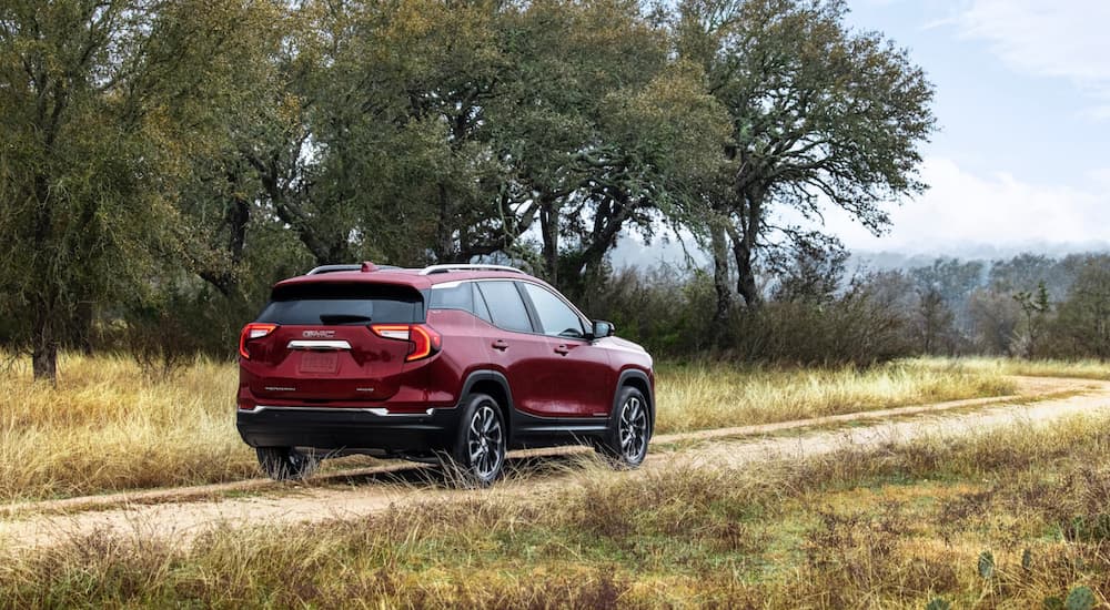 A red 2022 GMC Terrain is shown driving on a dirt path past a row of trees.