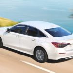 A white 2022 Honda Civic XL is shown driving past a lake during a 2022 Honda Civic vs 2022 Toyota Corolla comparison.