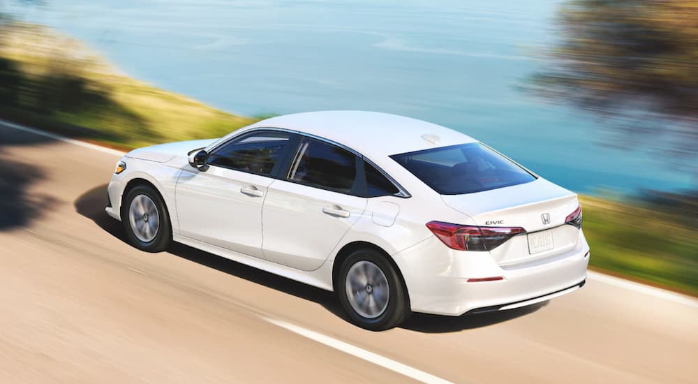 A white 2022 Honda Civic XL is shown driving past a lake during a 2022 Honda Civic vs 2022 Toyota Corolla comparison.