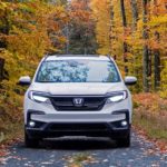 A white 2022 Honda Pilot Black Edition is shown from the front driving down a forest road.