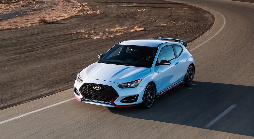 A light blue 2022 Hyundai Veloster N is shown driving on a road during a 2022 Volkswagen Golf R vs 2022 Hyundai Veloster N comparison.