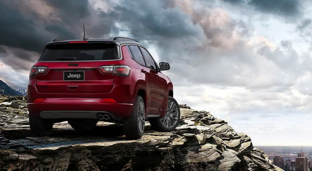 A red 2022 Jeep Compass is shown from the rear on top of a rocky mountain.