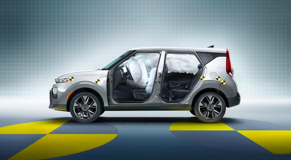 A silver 2022 Kia Soul with safety decals is shown from the side with the airbags deployed.