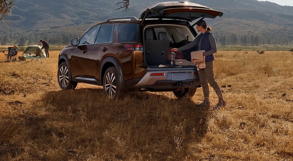 A woman is shown by the open tailgate of a maroon 2022 Nissan Pathfinder.