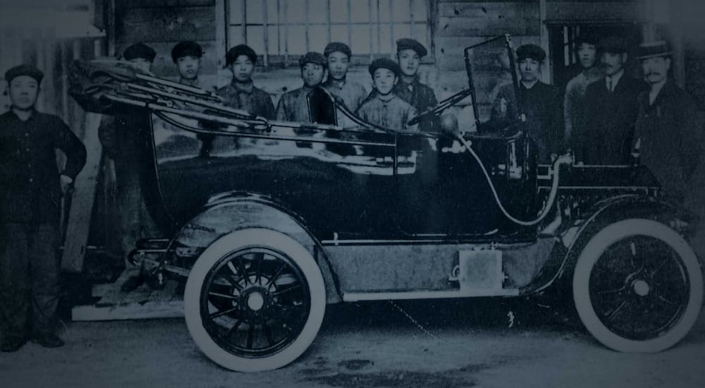 A 1914 Datsun DAT-Car is shown from the side surrounded by Datsun workers.