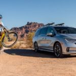 A family is shown riding bikes near a silver 2022 Honda Odyssey Elite in a desert area.