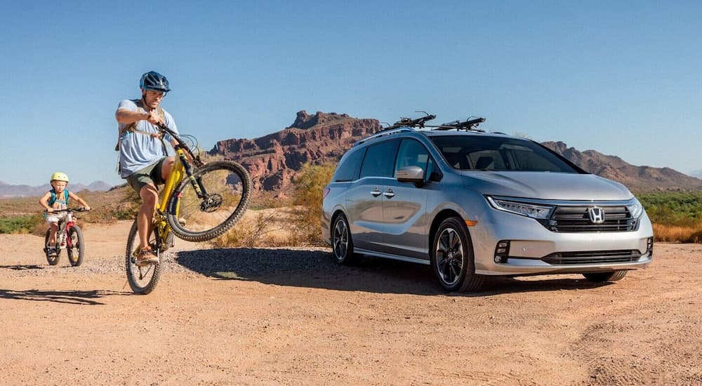 A family is shown riding bikes near a silver 2022 Honda Odyssey Elite in a desert area.