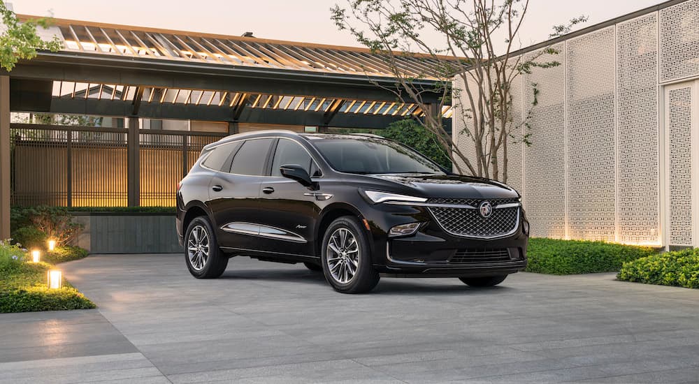 A black 2022 Buick Enclave is shown from the side parked in front of a modern house.