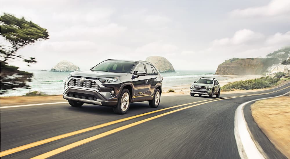 A black and a silver 2020 Toyota RAV4 are shown driving on a coastal road.