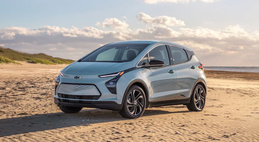 A light blue 2022 Chevy Bolt EV is shown from the side parked on the beach.