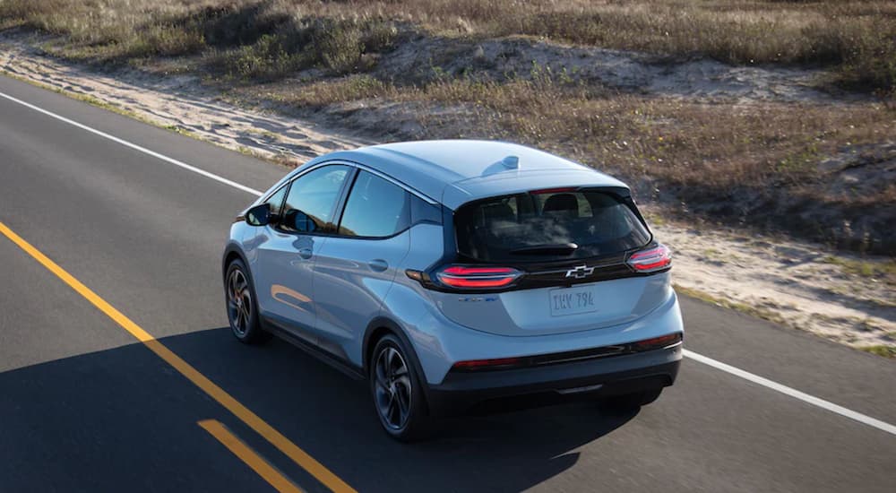 A light blue 2022 Chevy Bolt EV is shown from the rear driving on an open road.