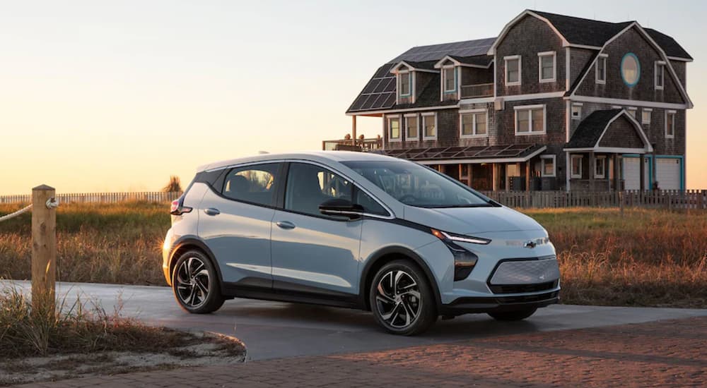 A light blue 2022 Chevy Bolt EV is shown from the side parked in front of a modern beach house.